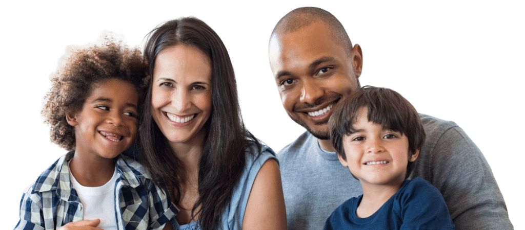 A smiling family of four poses for a photo. Two children, one with curly hair wearing a checked shirt and the other with straight hair in a blue shirt, sit in the front, while an adult man and woman stand behind them, both also smiling.