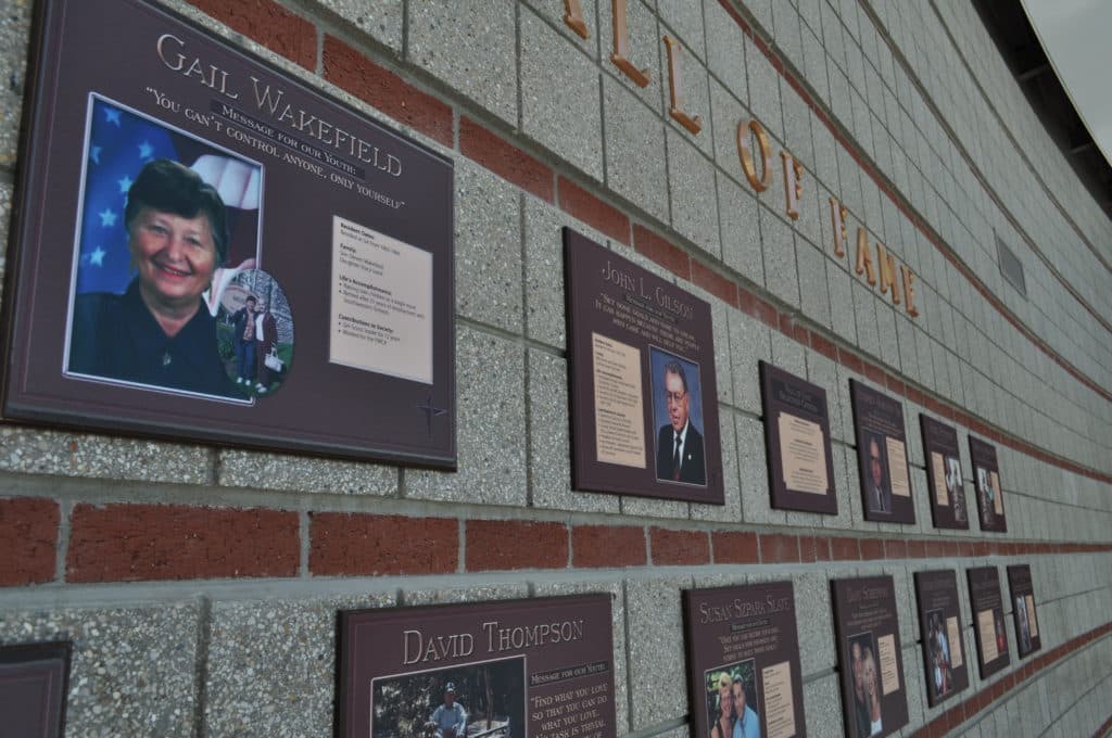 A wall plaque display featuring photographs and information about individuals, including Gail Wakefield and David Thompson. The heading above reads "Hall of Fame," with a decorative arrangement of memorial plaques on a textured wall.
